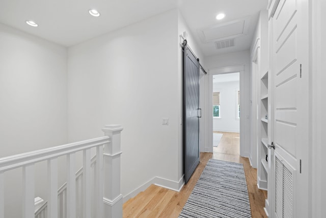 hallway featuring a barn door, light wood-style flooring, visible vents, and recessed lighting