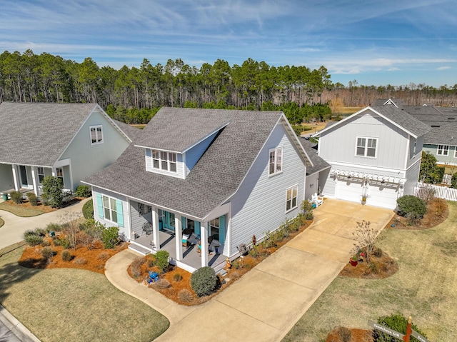 traditional home with a porch, an attached garage, a shingled roof, fence, and concrete driveway