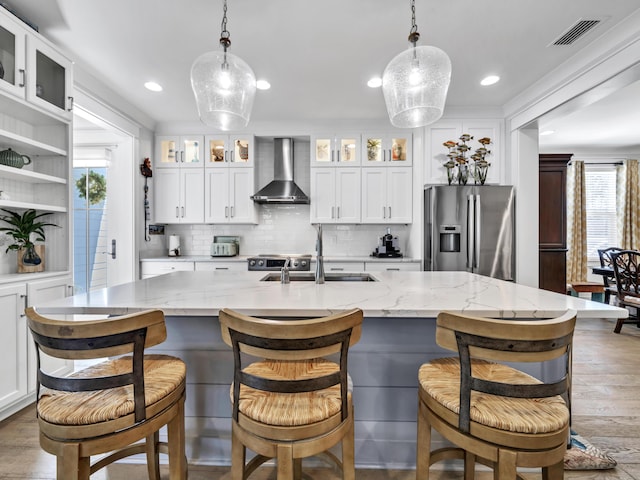 kitchen featuring visible vents, wall chimney exhaust hood, appliances with stainless steel finishes, wood finished floors, and a sink