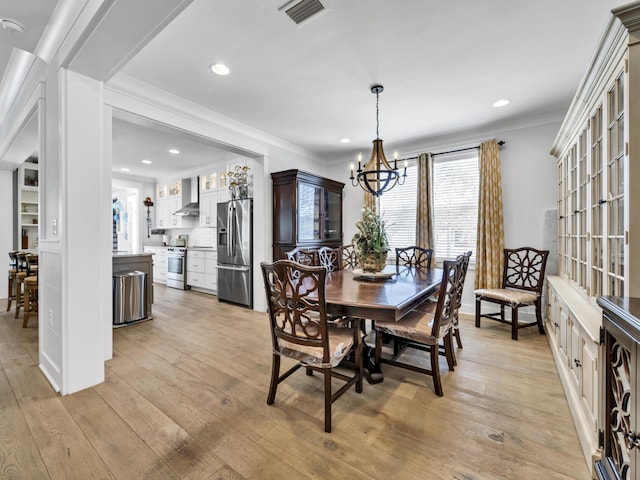 dining space with visible vents, ornamental molding, light wood-style flooring, and a notable chandelier