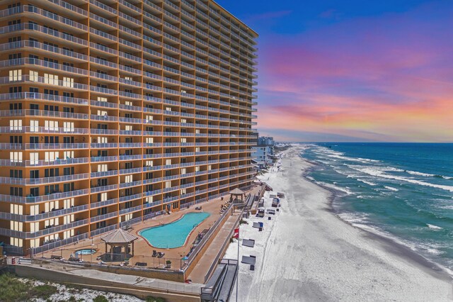 aerial view at dusk featuring a view of the beach and a water view