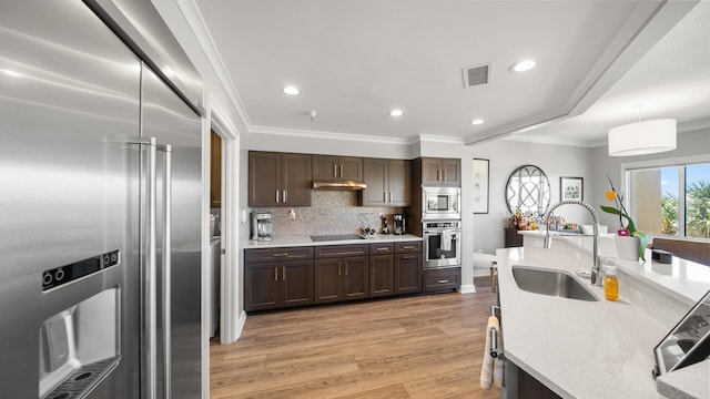 kitchen featuring built in appliances, under cabinet range hood, visible vents, hanging light fixtures, and ornamental molding