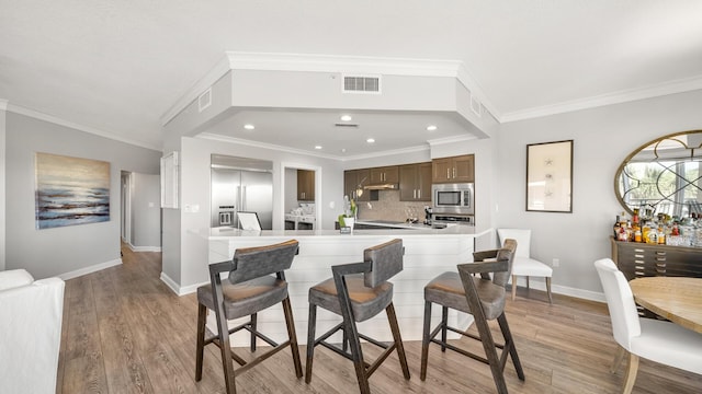 kitchen featuring light wood finished floors, light countertops, visible vents, built in appliances, and a peninsula