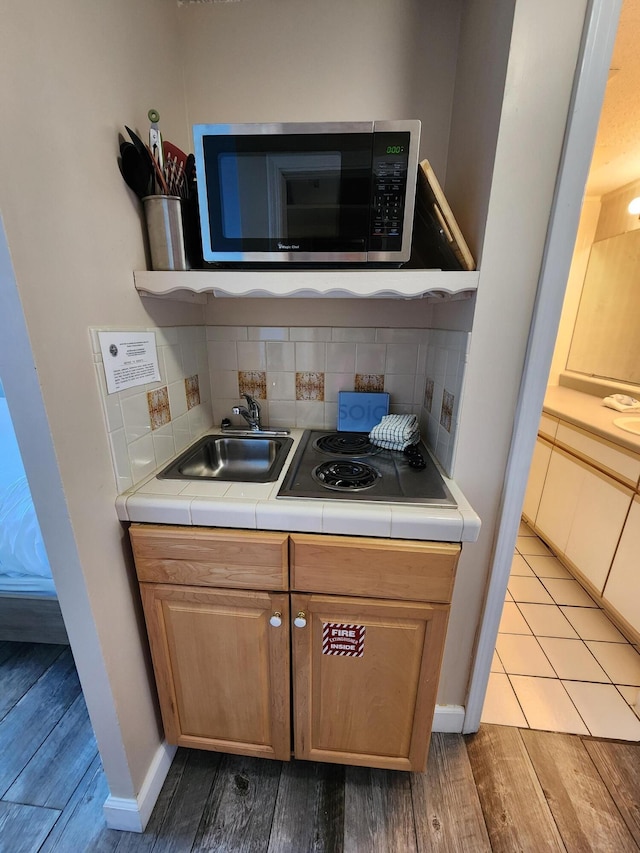 kitchen featuring tile countertops, stainless steel microwave, a sink, and decorative backsplash