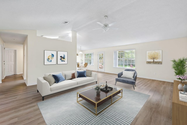 living room featuring light wood-style floors, baseboards, visible vents, and vaulted ceiling