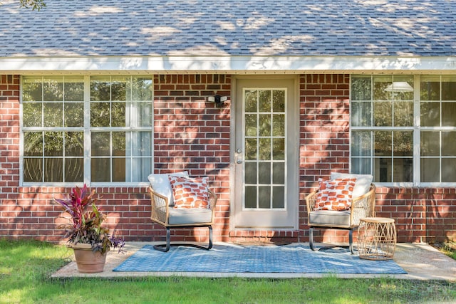 doorway to property featuring a shingled roof and brick siding