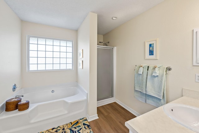 bathroom featuring a textured ceiling, wood finished floors, a stall shower, and a garden tub