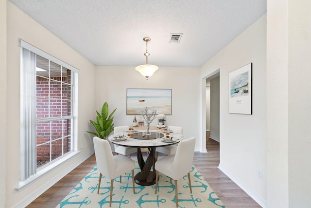 dining room featuring a textured ceiling, wood finished floors, visible vents, and baseboards