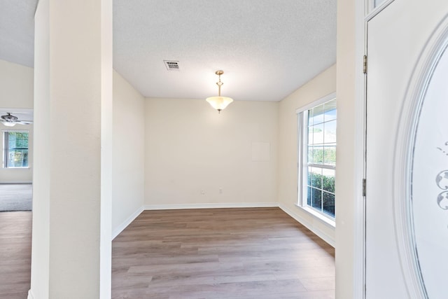 spare room with a textured ceiling, wood finished floors, a ceiling fan, visible vents, and baseboards