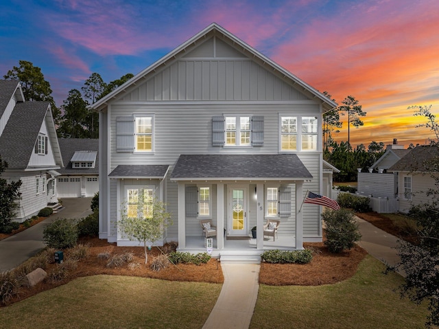 view of front facade featuring a shingled roof, covered porch, board and batten siding, a garage, and driveway