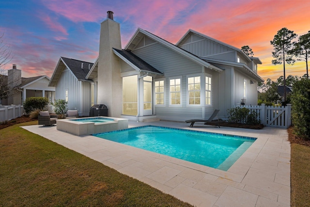 back of property at dusk with a chimney, board and batten siding, a gate, a patio area, and fence