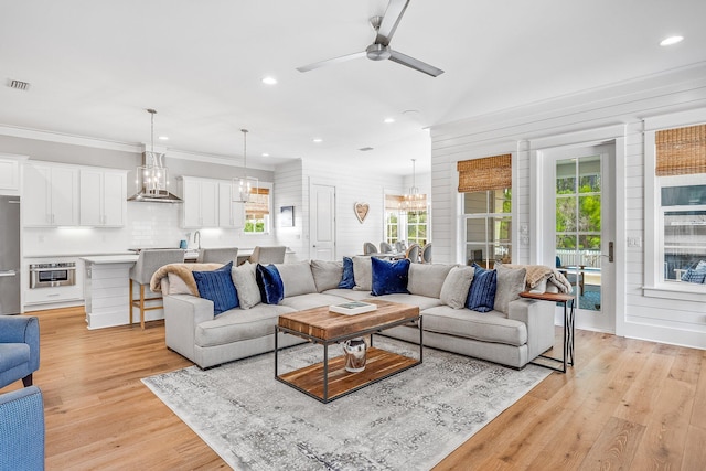 living room with ceiling fan with notable chandelier, visible vents, light wood-style flooring, and crown molding