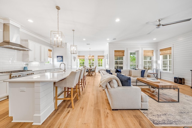 kitchen featuring gas cooktop, a sink, white cabinets, light wood-type flooring, and wall chimney exhaust hood