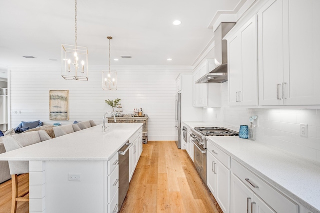 kitchen featuring a breakfast bar area, stainless steel appliances, white cabinetry, open floor plan, and wall chimney range hood