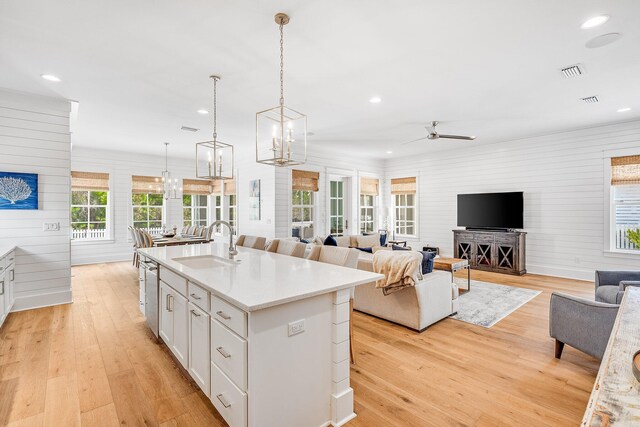 kitchen featuring an island with sink, open floor plan, light wood-type flooring, white cabinetry, and a sink