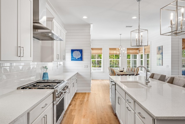 kitchen featuring stainless steel appliances, a sink, light wood-style floors, wall chimney exhaust hood, and tasteful backsplash