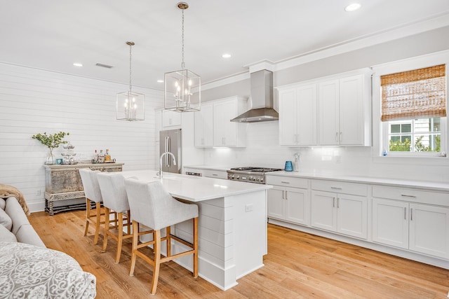 kitchen with visible vents, light countertops, light wood-type flooring, wall chimney range hood, and a kitchen bar