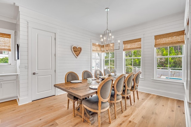 dining area featuring light wood-type flooring, a notable chandelier, and wooden walls