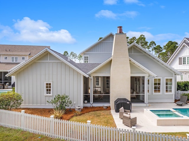 rear view of property with a sunroom, a chimney, board and batten siding, and a patio