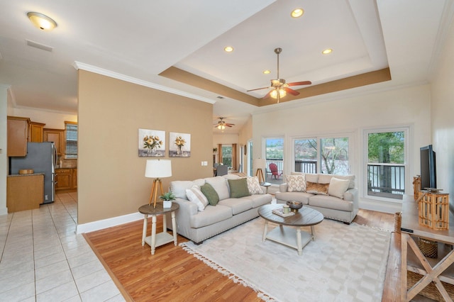 living room with ornamental molding, a tray ceiling, light wood-type flooring, and baseboards