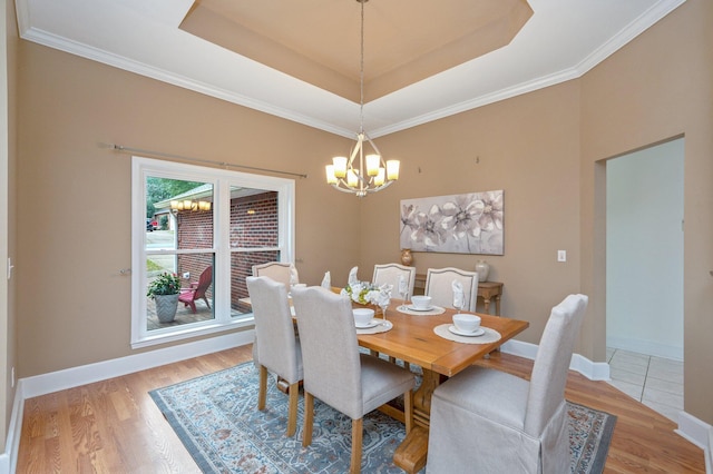 dining room with light wood-type flooring, baseboards, a tray ceiling, and a notable chandelier