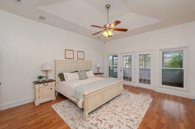 bedroom featuring access to outside, baseboards, light wood-style flooring, and a raised ceiling