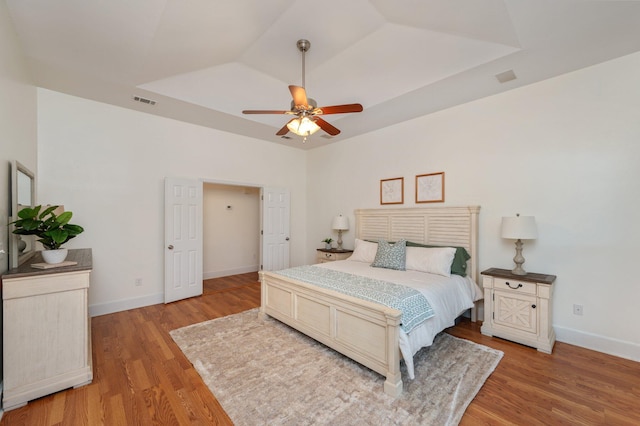 bedroom with light wood-type flooring, a tray ceiling, visible vents, and baseboards