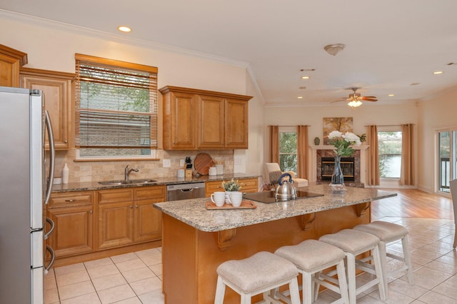 kitchen with brown cabinets, stainless steel appliances, tasteful backsplash, a high end fireplace, and a sink