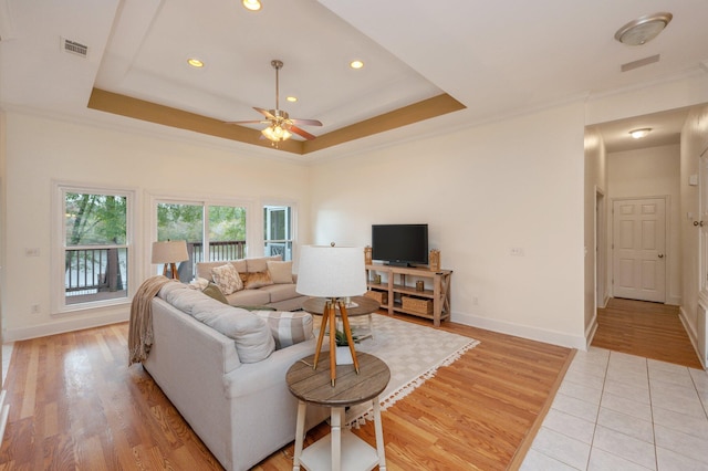 living area with baseboards, ornamental molding, a raised ceiling, and light wood-style floors