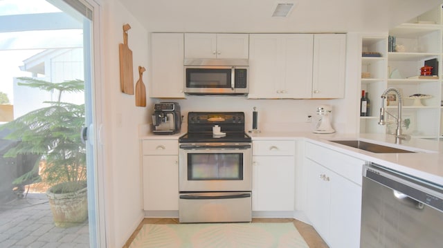 kitchen featuring stainless steel appliances, light countertops, a sink, and white cabinetry