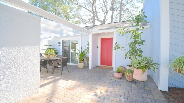 view of exterior entry featuring outdoor dining area, a patio area, and a pergola