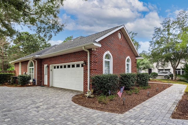 view of home's exterior featuring brick siding, a shingled roof, decorative driveway, and a garage