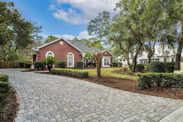 view of front of house featuring brick siding, decorative driveway, and fence