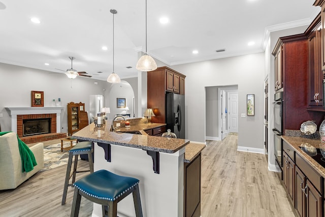 kitchen with a breakfast bar area, a peninsula, a fireplace, a sink, and black appliances