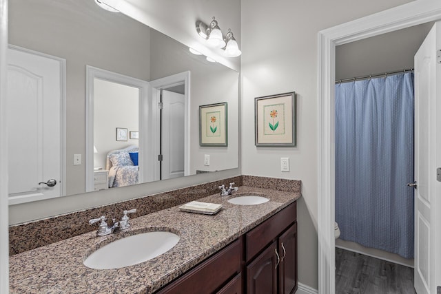 bathroom featuring double vanity, connected bathroom, wood finished floors, and a sink