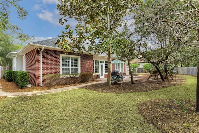 view of front of house with fence, roof with shingles, a front yard, brick siding, and a patio area