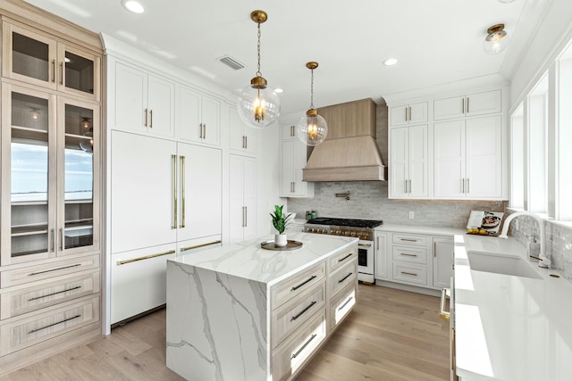 kitchen featuring visible vents, premium appliances, a kitchen island, custom range hood, and a sink