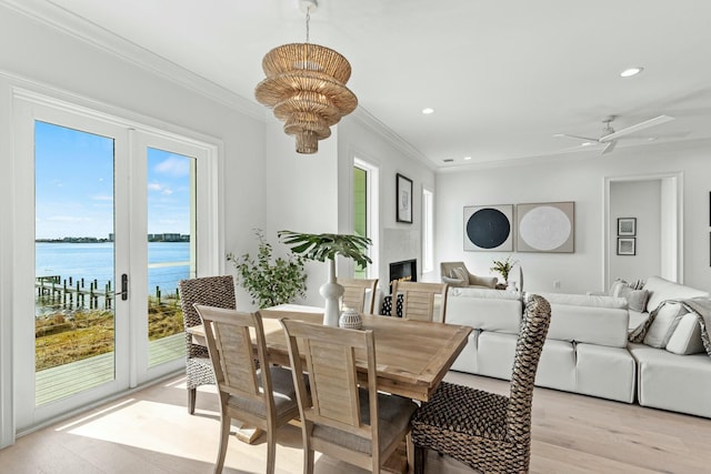 dining room featuring a water view, a lit fireplace, crown molding, and recessed lighting