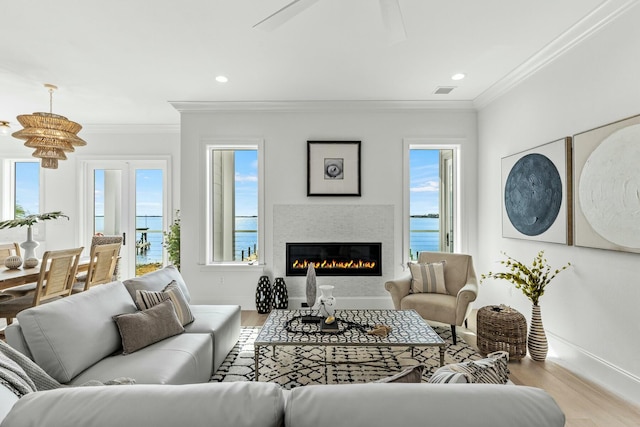 living area featuring ornamental molding, a glass covered fireplace, baseboards, and wood finished floors