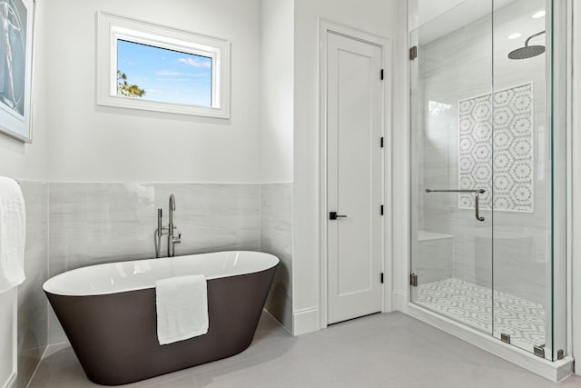 full bathroom featuring tile walls, a freestanding tub, a wainscoted wall, and a shower stall