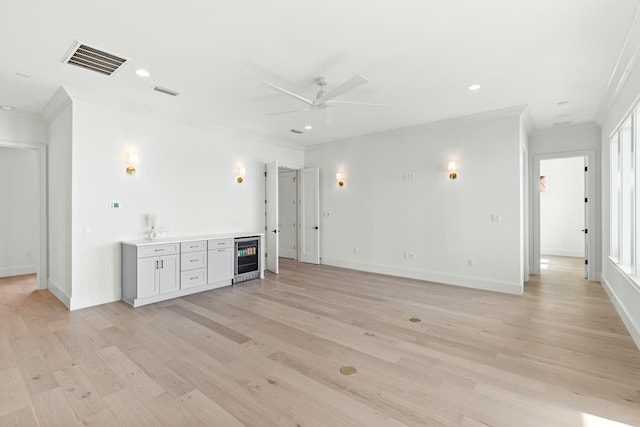 unfurnished living room featuring wine cooler, visible vents, baseboards, light wood-style floors, and ornamental molding