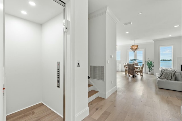 hall with stairs, light wood-type flooring, visible vents, and elevator