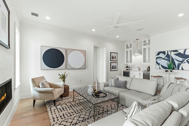 living room featuring light wood-style flooring, recessed lighting, bar area, a lit fireplace, and crown molding