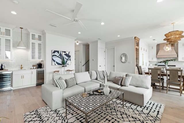 living room featuring light wood-type flooring, beverage cooler, ornamental molding, and recessed lighting