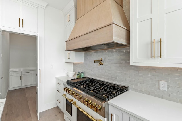 kitchen featuring custom exhaust hood, light countertops, white cabinetry, light wood-type flooring, and double oven range