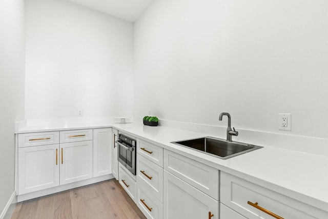 kitchen with oven, a sink, white cabinets, light countertops, and light wood finished floors