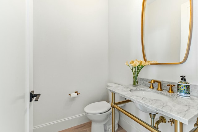 bathroom with toilet, baseboards, a sink, and wood finished floors