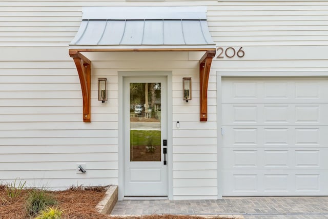 entrance to property with a garage, a standing seam roof, and metal roof