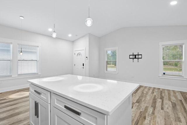 kitchen with baseboards, white cabinets, vaulted ceiling, light wood-style floors, and pendant lighting