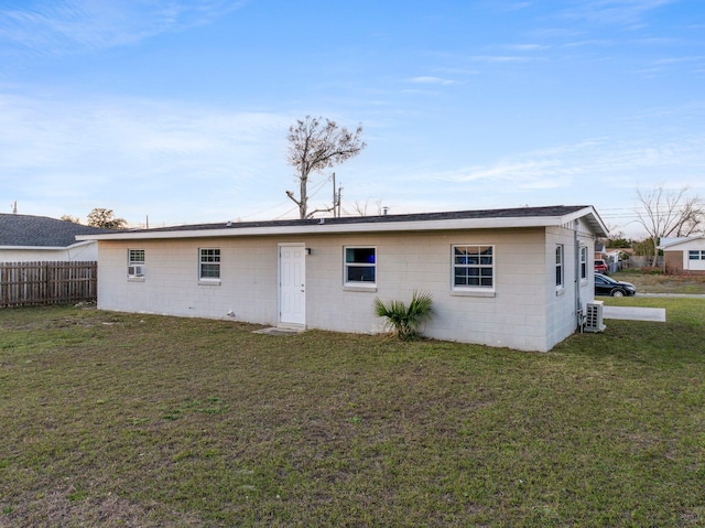 rear view of house featuring concrete block siding, a lawn, and fence